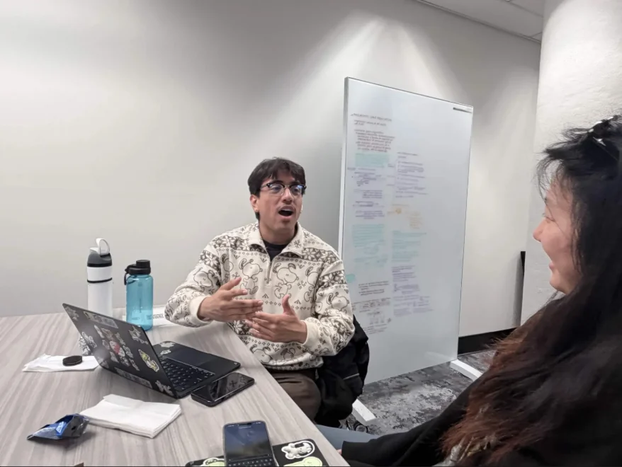 Jared gesturing while interviewing a participant across a table, with a laptop and notes in front of him